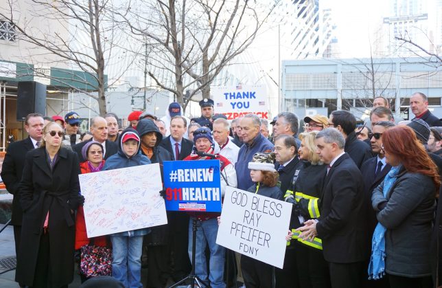 John Feal, surrounded by politicians and 9/11 advocates and two young boys holding get well wishes for Ray Pfeifer, speaks at the victory press conference in front of One World Trade Center on December 19, 2015, a day after the reauthorization of the James Zadroga 9/11 Health and Compensation Act of 2010 which will provide healthcare and compensation to responders and survivors from 9/11. Photo by: Suneet Mahandru